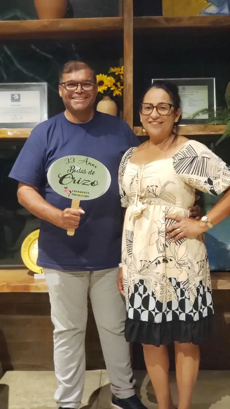Casal comemorando 33 anos de casados na Viagem das Bodas, com a placa do Casamento Fortalecido