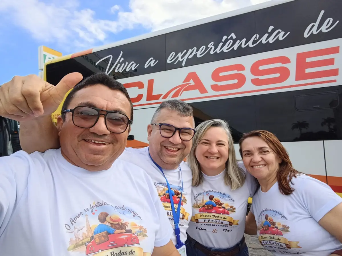 Edson, Maclania e um casal amigo com as camisetas da Viagem das Bodas, sorrindo na frente do ônibus