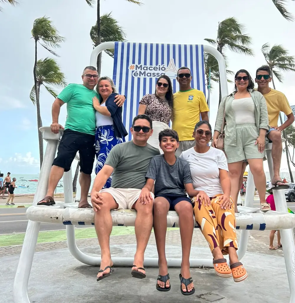 Turma de clientes da Logos sentada na cadeira gigante da orla de Maceió